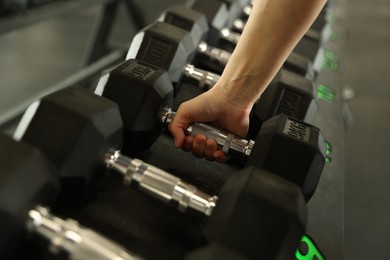 Woman taking rubber hex dumbbell in gym, closeup