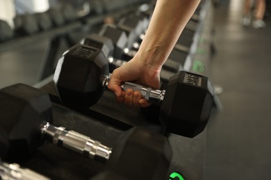 Photo of Woman taking rubber hex dumbbell in gym, closeup