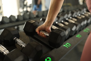 Photo of Woman taking rubber hex dumbbell in gym, closeup