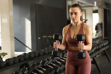 Athletic woman training with dumbbells in gym. Space for text