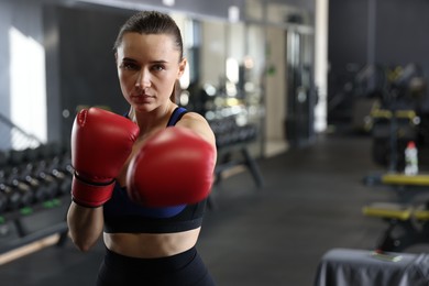 Athletic woman wearing boxing gloves training in gym. Space for text