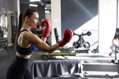 Athletic woman wearing boxing gloves training in gym. Space for text