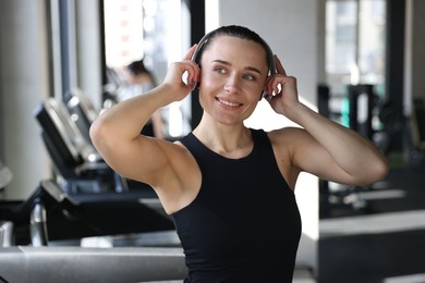 Photo of Smiling woman wearing headphones listening to music in gym