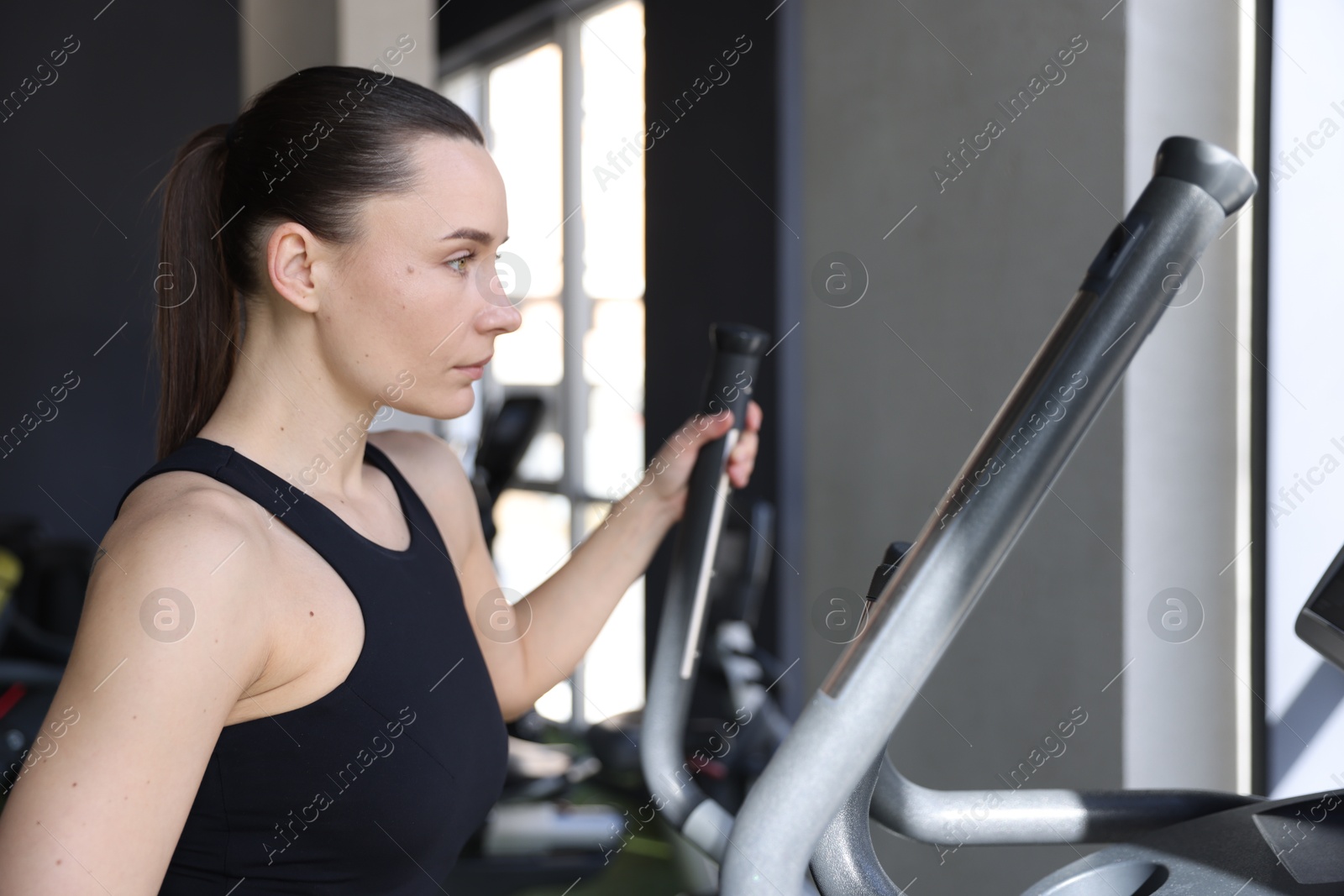 Photo of Athletic woman training on elliptical machine in gym