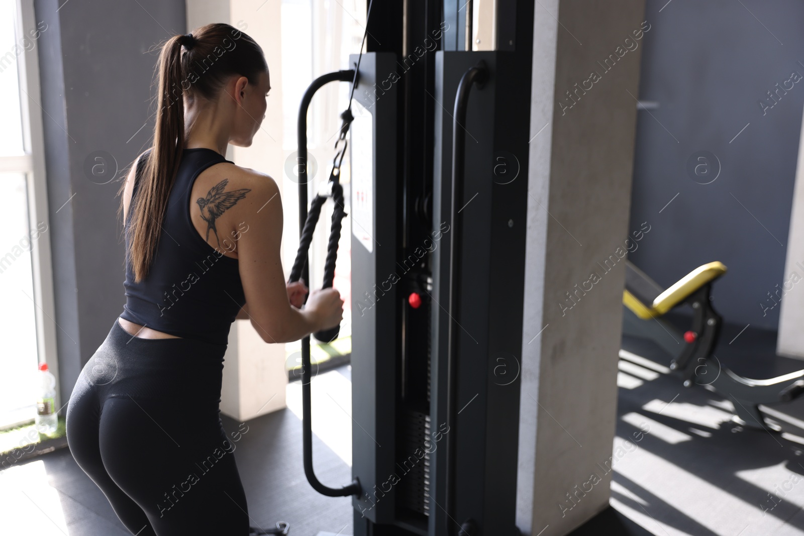 Photo of Athletic woman training on pulley machine in gym, back view