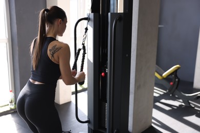 Athletic woman training on pulley machine in gym, back view