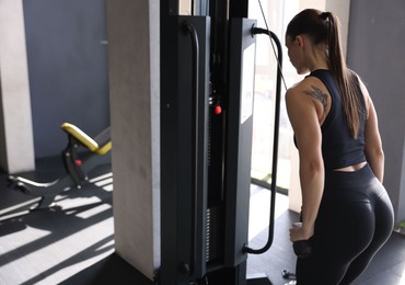 Athletic woman training on pulley machine in gym, back view