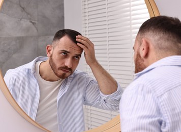 Photo of Baldness problem. Man with receding hairline near mirror in bathroom