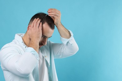 Baldness treatment. Man applying serum onto hair on light blue background. Space for text