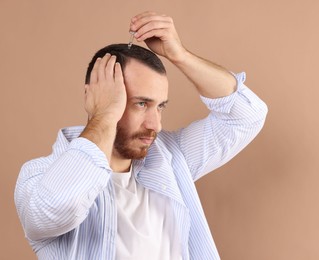 Photo of Baldness treatment. Man applying serum onto hair on beige background