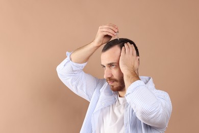 Baldness treatment. Man applying serum onto hair on beige background