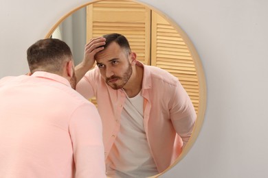 Photo of Baldness problem. Man with receding hairline near mirror at home. Space for text