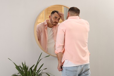 Baldness problem. Man with receding hairline near mirror at home, back view