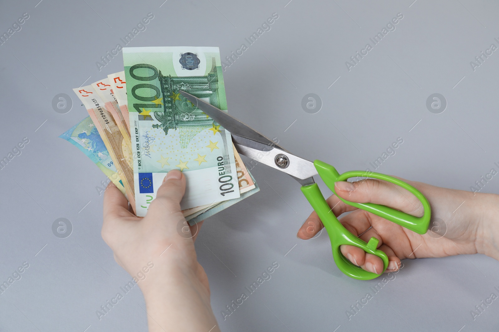 Photo of Woman cutting euro banknotes on gray background, closeup