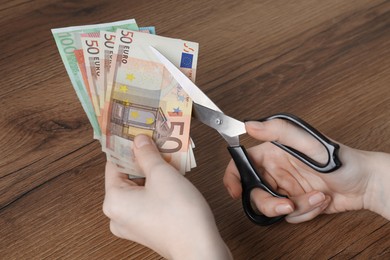 Woman cutting euro banknotes at wooden table, closeup