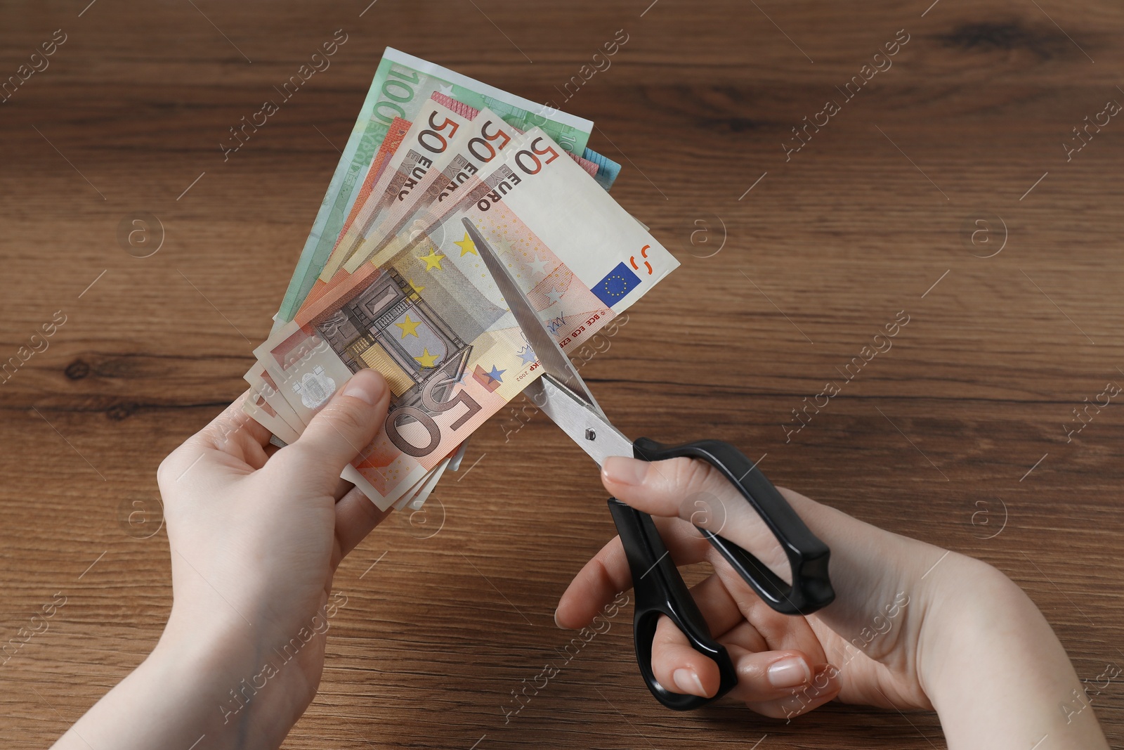 Woman cutting euro banknotes at wooden table, closeup Photo of Woman cutting euro banknotes at wooden table, closeup