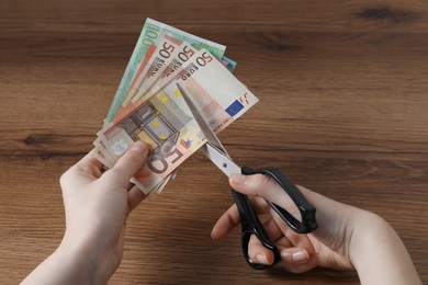 Photo of Woman cutting euro banknotes at wooden table, closeup