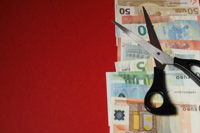 Photo of Euro banknotes and scissors on red background, closeup. Space for text