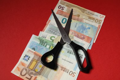 Photo of Euro banknotes and scissors on red background