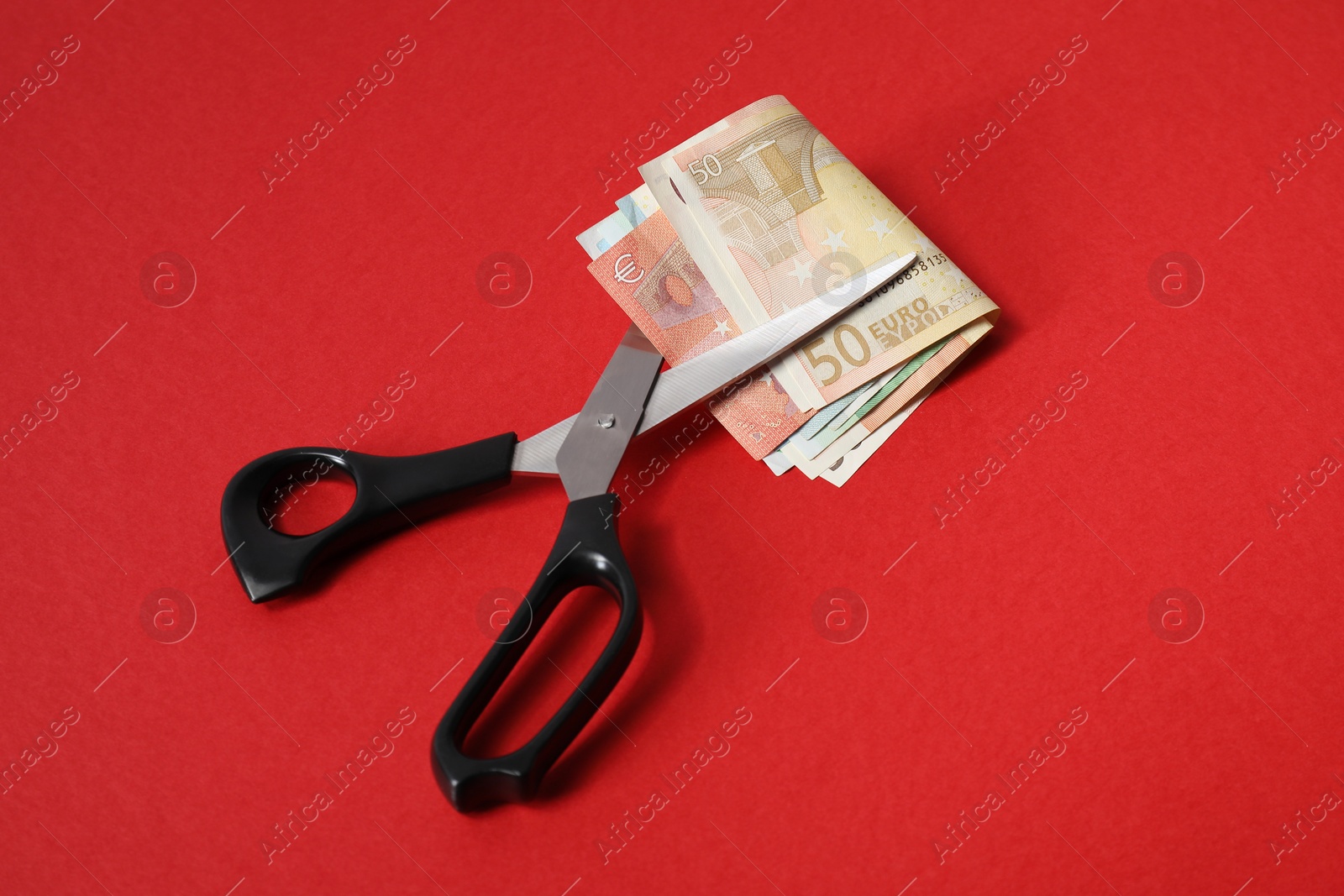 Photo of Euro banknotes and scissors on red background