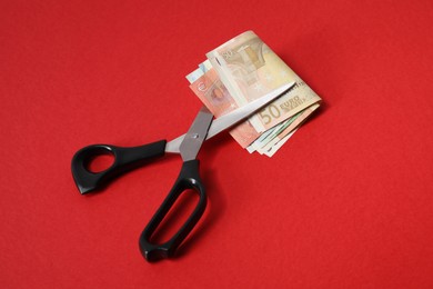 Euro banknotes and scissors on red background