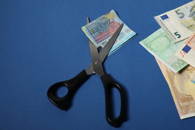 Photo of Scissors with euro banknotes on blue background, space for text