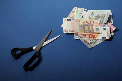 Euro banknote and scissors on blue background