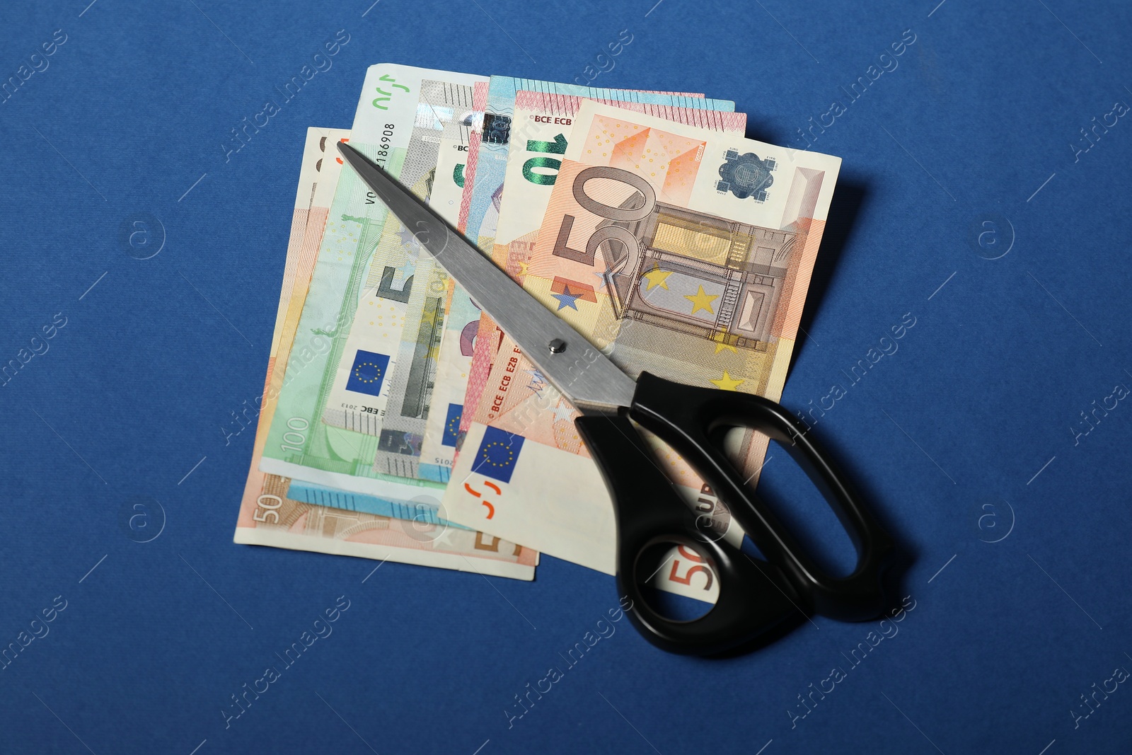 Photo of Euro banknote and scissors on blue background, top view