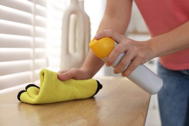 Photo of Woman using cleaning product while polishing wooden table with rag indoors, closeup