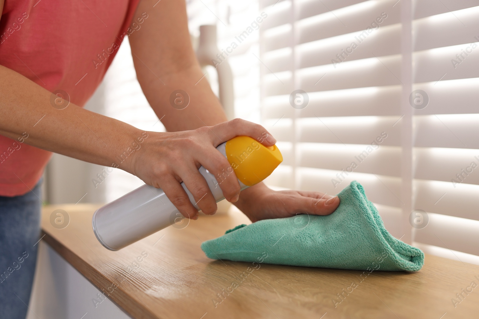 Photo of Woman using cleaning product while polishing wooden table with rag indoors, closeup