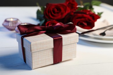 Photo of Beautiful table setting with romantic gift, flowers and burning candles on white wooden background, closeup