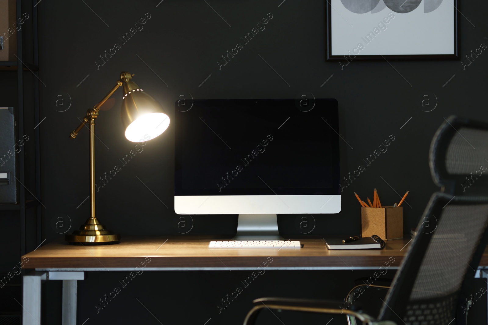 Comfortable workplace with computer and lamp on wooden desk at home office in evening Photo of Comfortable workplace with computer and lamp on wooden desk at home office in evening
