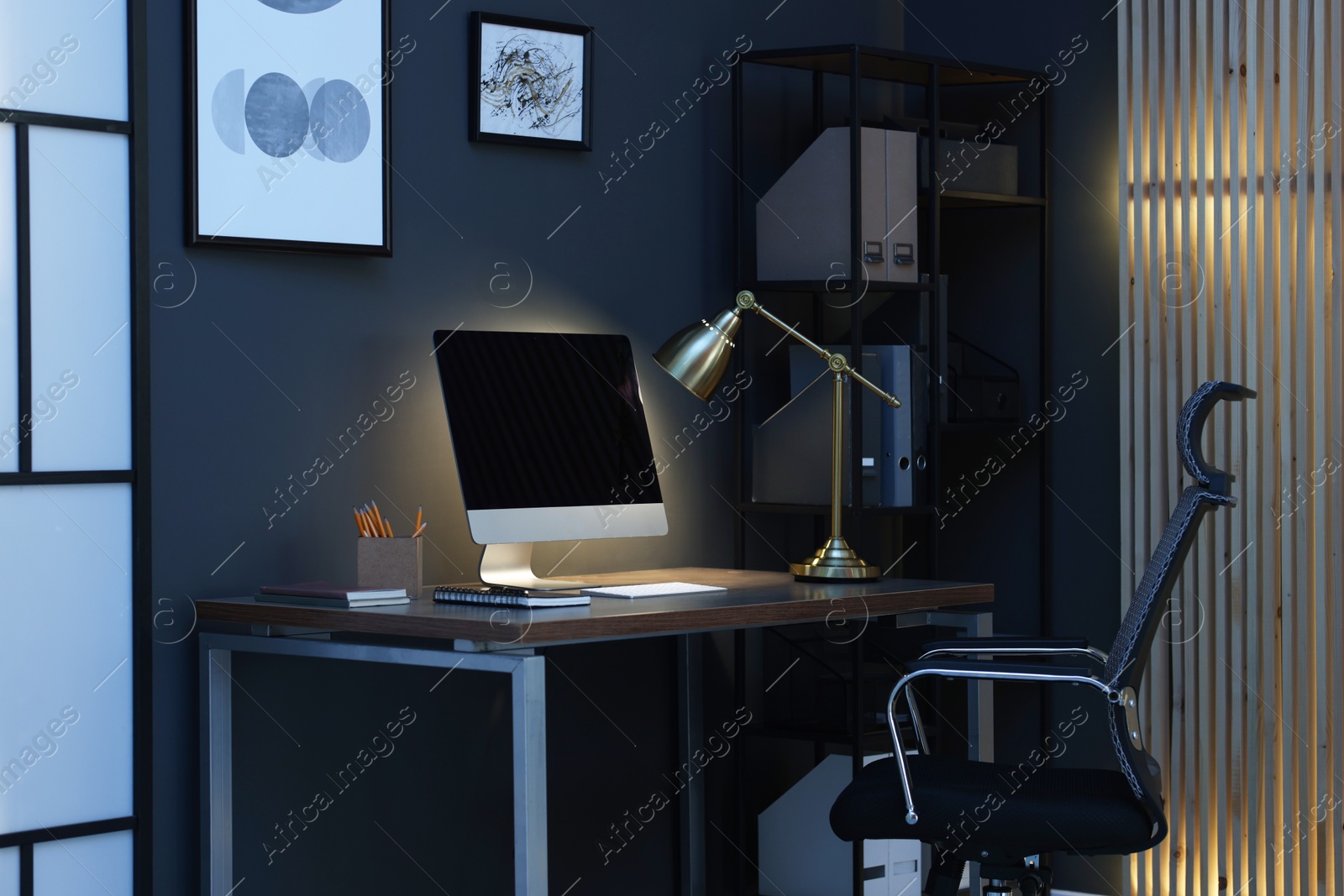 Comfortable workplace with computer and lamp on wooden desk at home office in evening Photo of Comfortable workplace with computer and lamp on wooden desk at home office in evening