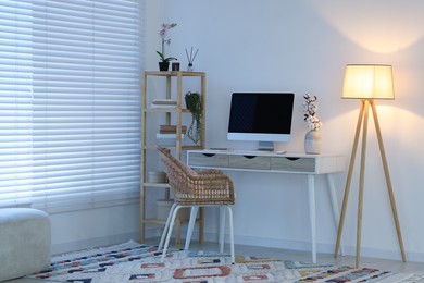 Photo of Comfortable workplace with computer on desk and floor lamp at home office in evening