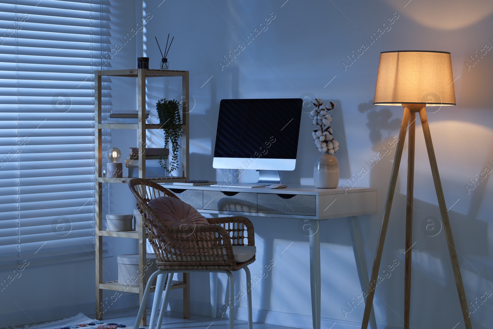 Comfortable workplace with computer on desk and floor lamp at home office in evening Photo of Comfortable workplace with computer on desk and floor lamp at home office in evening