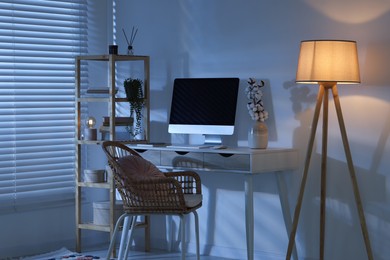 Photo of Comfortable workplace with computer on desk and floor lamp at home office in evening