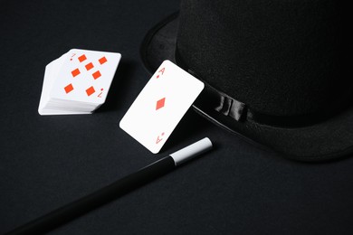 Photo of Playing cards, hat and magic wand on black background, closeup