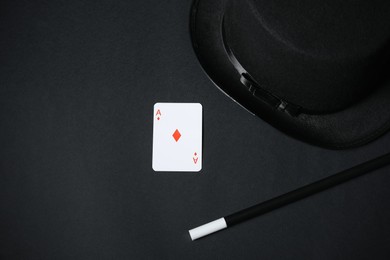 Photo of Playing card, hat and magic wand on black background, top view. Space for text