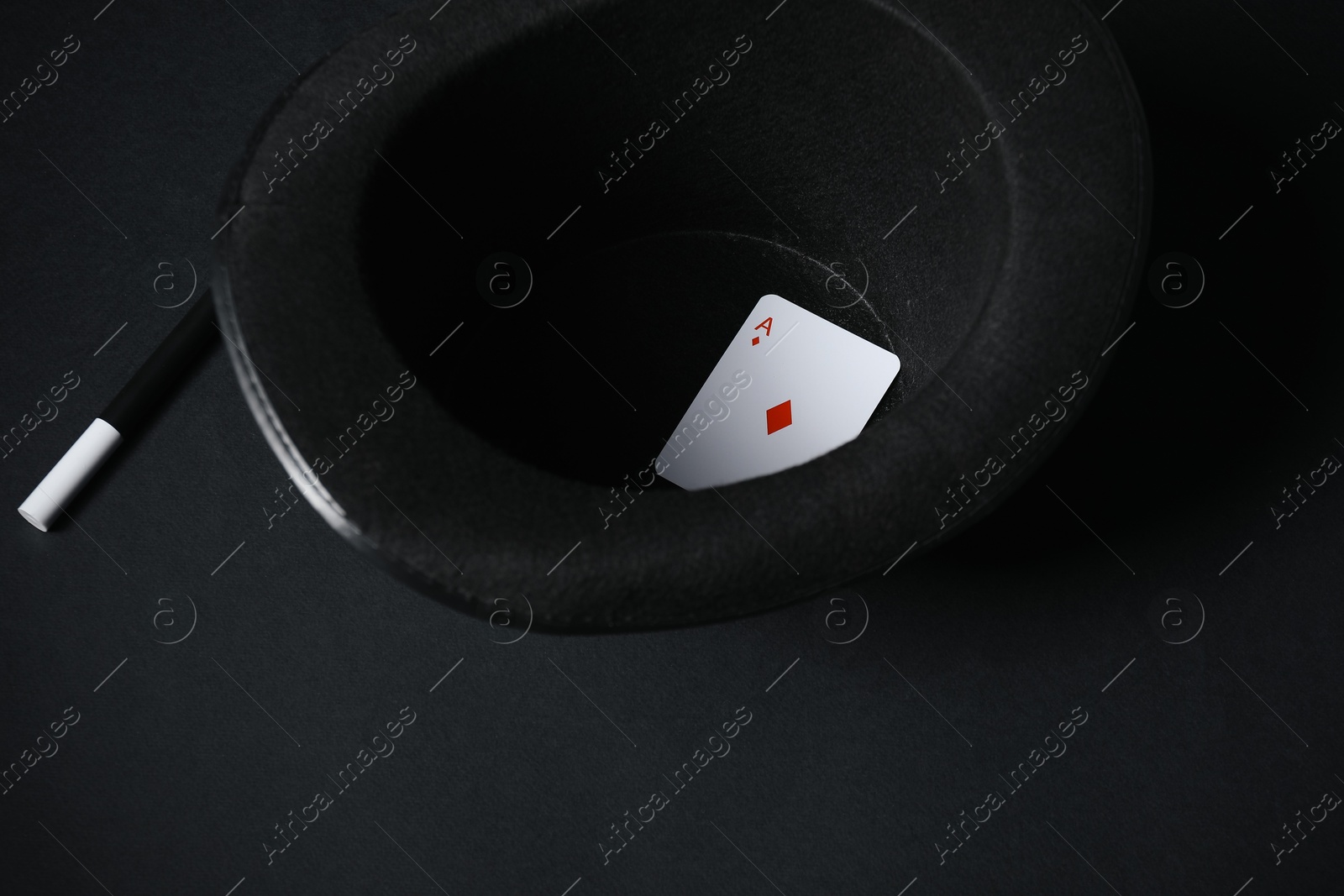 Photo of Playing card, hat and magic wand on black background, closeup