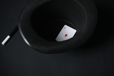 Playing card, hat and magic wand on black background, closeup