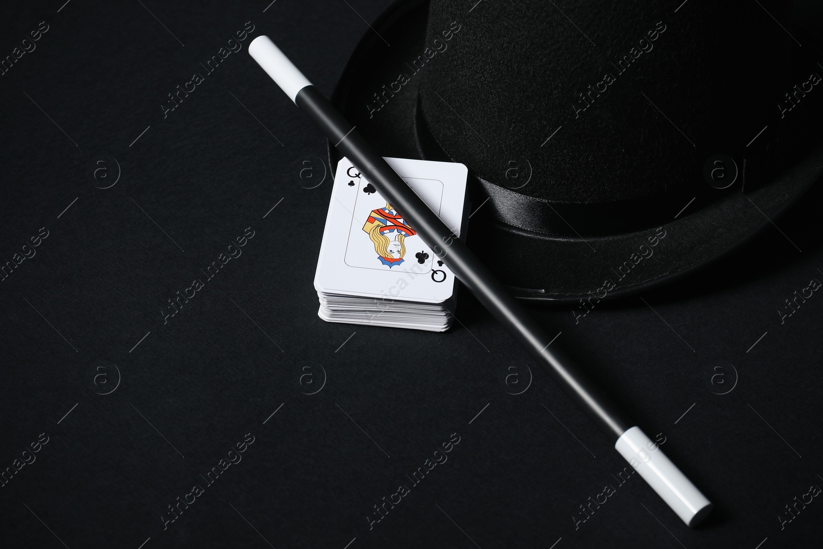 Photo of Playing cards, hat and magic wand on black background, closeup. Space for text