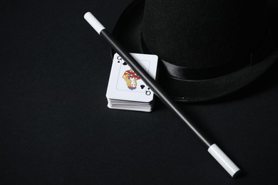 Playing cards, hat and magic wand on black background, closeup. Space for text