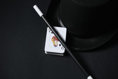 Photo of Playing cards, hat and magic wand on black background, closeup