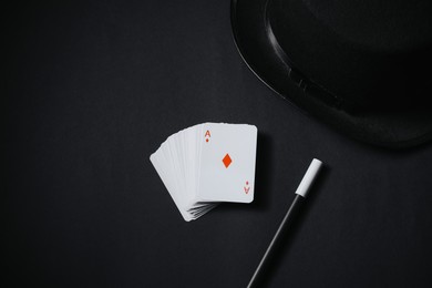 Playing cards, hat and magic wand on black background, top view