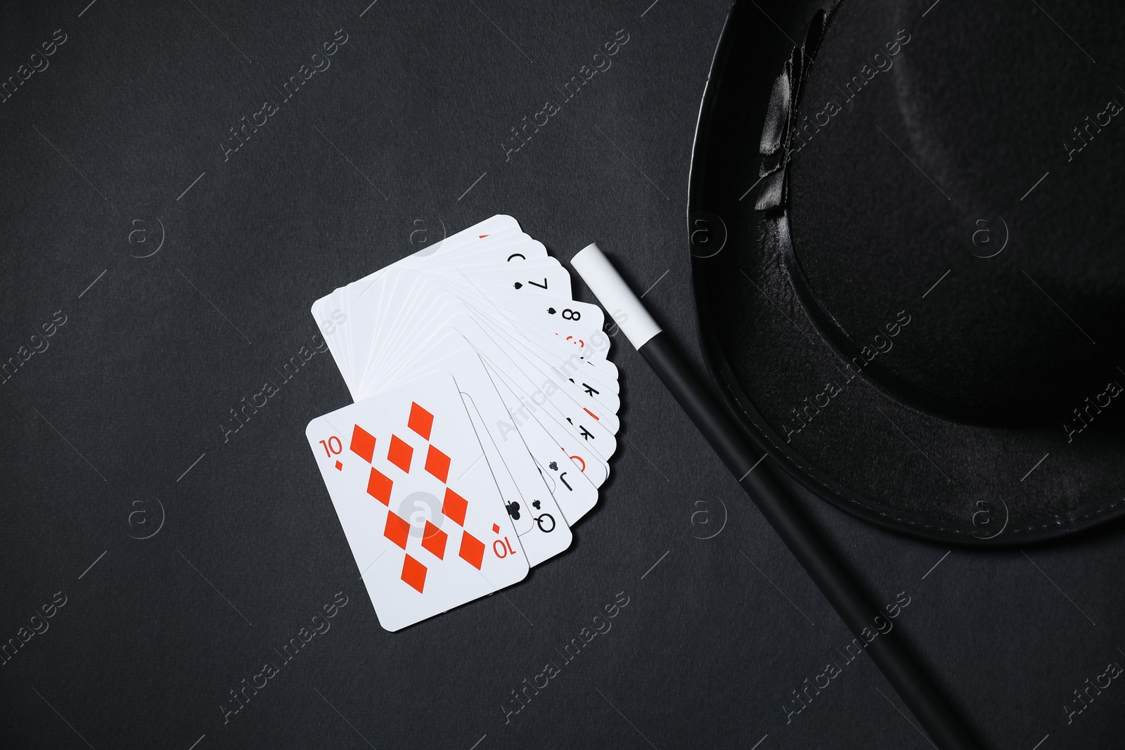 Photo of Playing cards, hat and magic wand on black background, top view