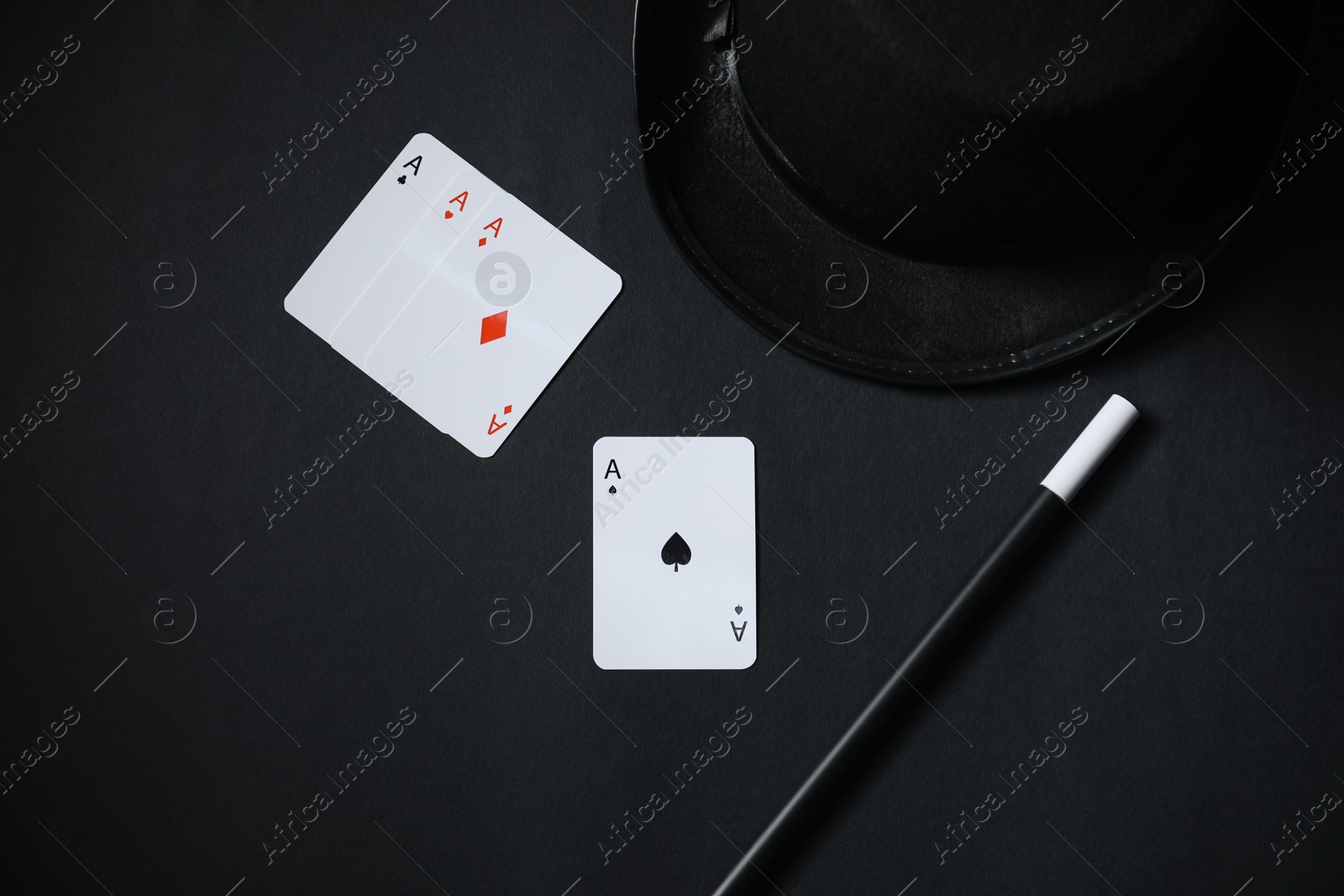 Photo of Playing cards, hat and magic wand on black background, top view