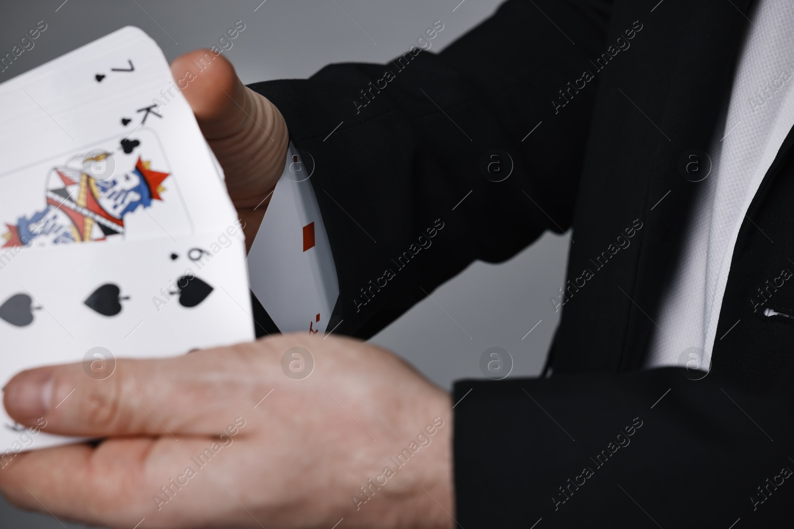 Photo of Illusionist shuffling playing cards on grey background, closeup