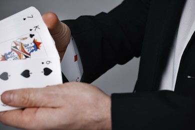 Photo of Illusionist shuffling playing cards on grey background, closeup