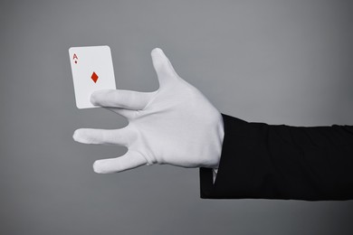 Photo of Illusionist with playing card on grey background, closeup