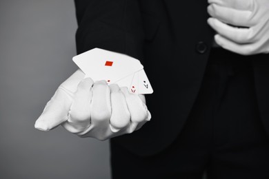 Illusionist taking playing cards out of sleeve on grey background, closeup